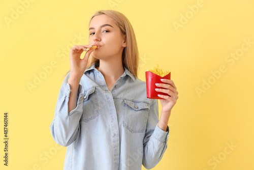 Young woman eating french fries on yellow background