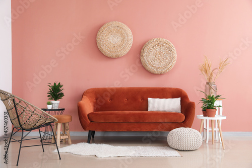 Stylish orange sofa with houseplants and wicker armchair in modern interior of living room