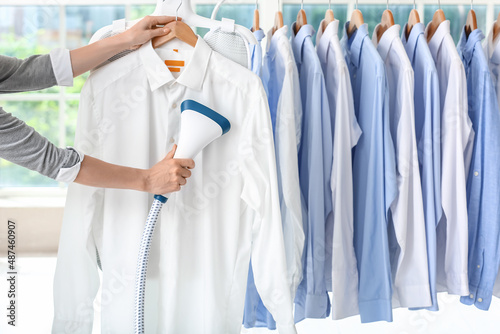 Woman ironing shirt with steam at dry-cleaning