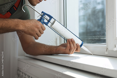 Foto Construction worker sealing window with caulk indoors, closeup