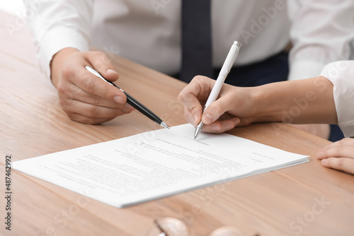 Businesspeople signing contract at wooden table, closeup