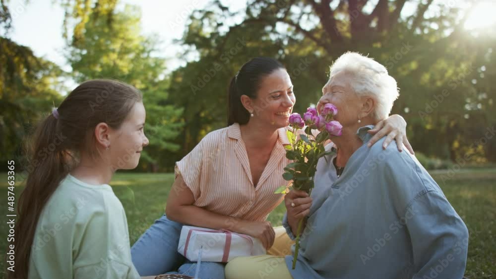 Small girl with mother giving cake and flowers to grandmother in a park, celebrating birthday. Small girl with mother giving cake and flowers to grandmother in a park, celebrating birthday.