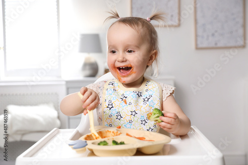 Cute little baby eating food in high chair at home