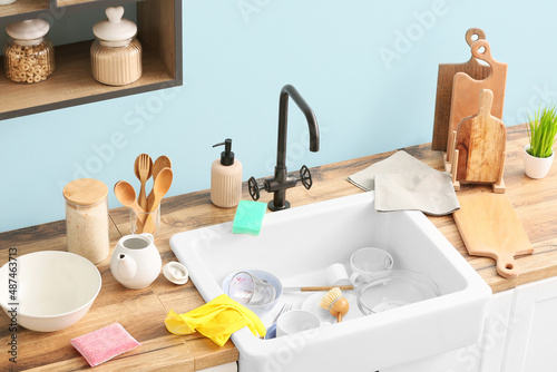 Fototapeta Naklejka Na Ścianę i Meble -  Ceramic sink with dirty dishes, cleaning supplies and kitchen utensils near blue wall