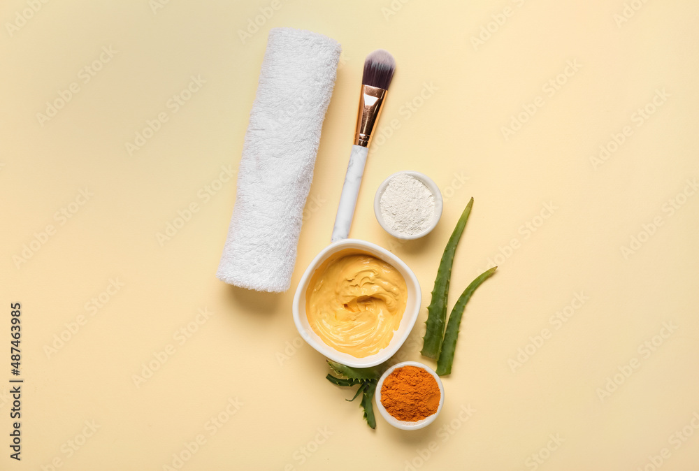 Bowls with turmeric mask, powder, makeup brush and aloe on beige background Bowls with turmeric mask, powder, makeup brush and aloe on beige background