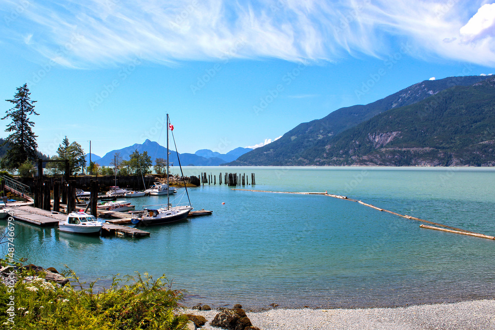 Harbour in Squamish BC Canada, overlooking turquoise blue clear water, blue cloud sky and boats in front of mountains 