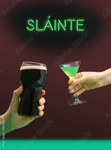 Party toasting modern concept. A man's hand with a pint of black stout beer glass and a girl's hand holds a martini glass with green cocktail. Irish gaelic slainte cheers in English green neon sign 