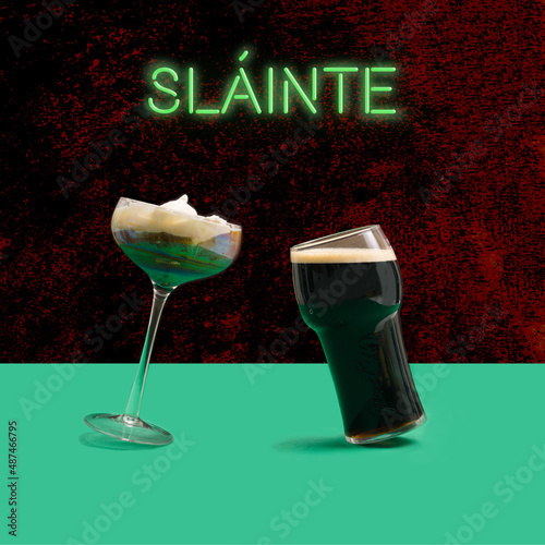 A unique Irish coffee glass and pint of black stout craft beer glass in front. Irish gaelic slainte  cheers in English green neon sign above. Dancing glasses modern concept. Plum concrete background. photo