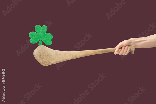 Man hands hold hurly sticks – hurleys. Green clover balancing  on top of it against a green background. Ireland traditional sport minimal concept. Plum background photo