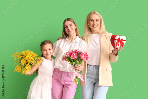 Young woman with her little daughter, mother and gifts on green background. International Women's Day