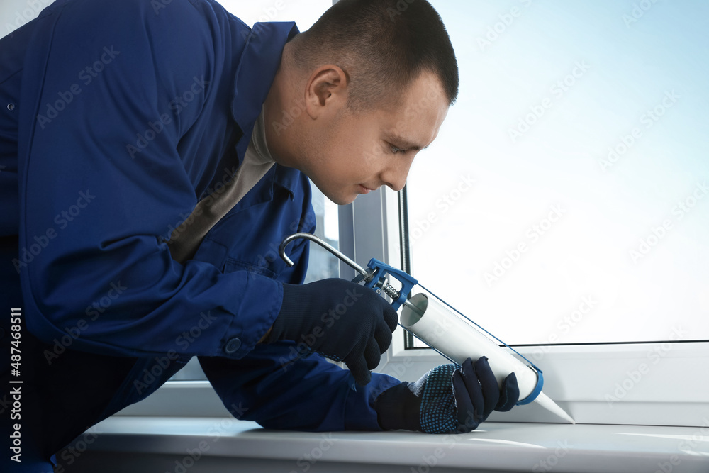 Construction worker sealing window with caulk indoors Construction worker sealing window with caulk indoors