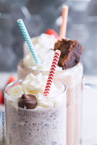 Glass mug of chocolate and strawberry and cookies and cream milkshake with rainbow straws on kitchen counter