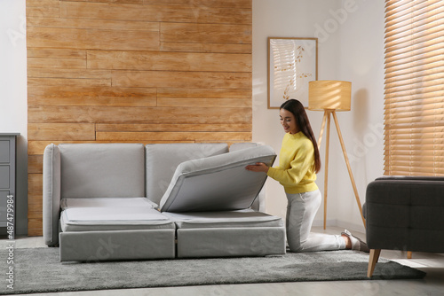 Young woman unfolding sofa into a bed in room. Modern interior photo