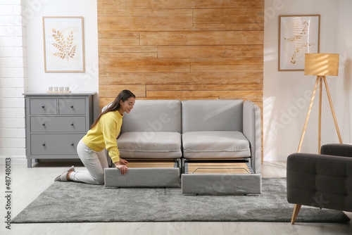 Fotografía Young woman unfolding sofa into a bed in room. Modern interior