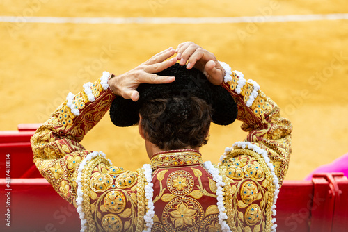 Bullfighter putting on the montera or the hat of bullfighting with his hands. Red bullfighter costume in the bullring in spain. Spanish tradition. Yellow sand 