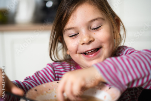 Close up of preschool girl portrait with funny expression eating soup at home 