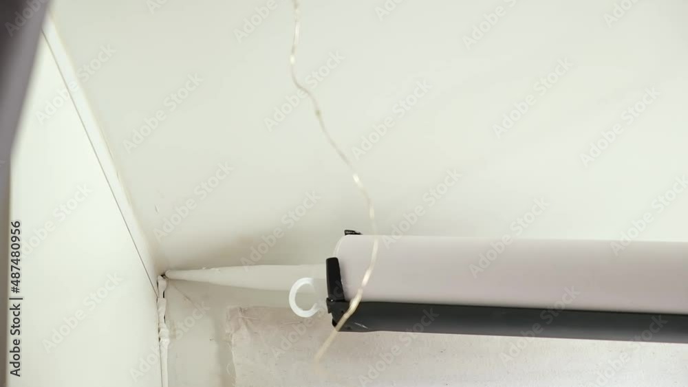 A man applies a sealant to the seam between the window and the sill from a tube of silicone
