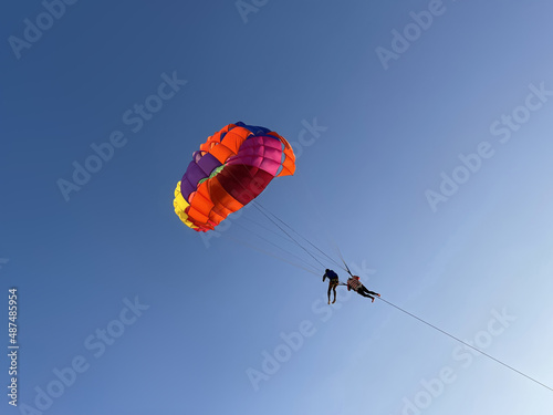 Parasailing, parascending, paraskiing, parakiting, Parachute with two people in the clear blue sky. Close-up, isolated, macro. Bright colors. Extreme sport. Flight in the skies. Soar at heaven. Fun