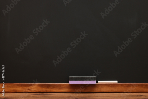 Fotografie Piece of chalk and duster on wooden table near blackboard, space for text