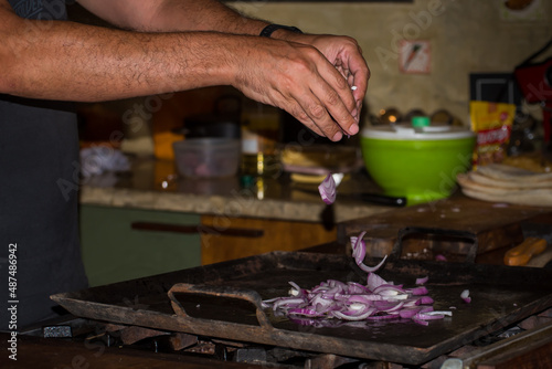 man's hands putting chopped onion on a kitchen griddle, background food