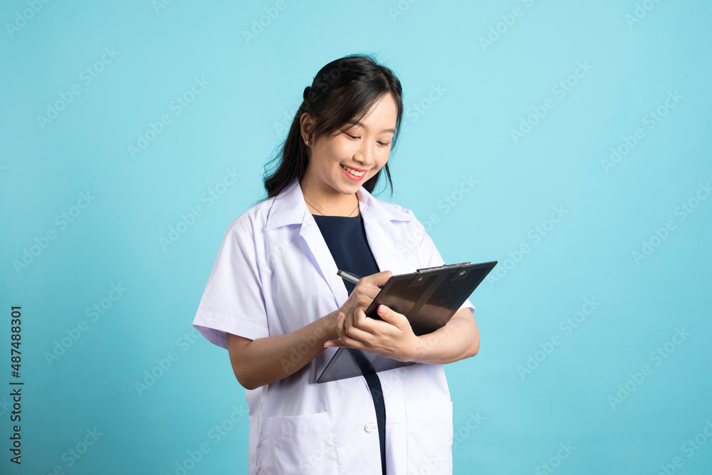 Asian doctor woman in medical uniform and clipboard smiling at camera standing on blue white background.