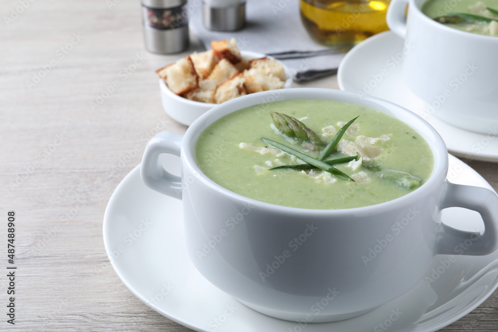 Delicious asparagus soup with green onion served on white wooden table Delicious asparagus soup with green onion served on white wooden table
