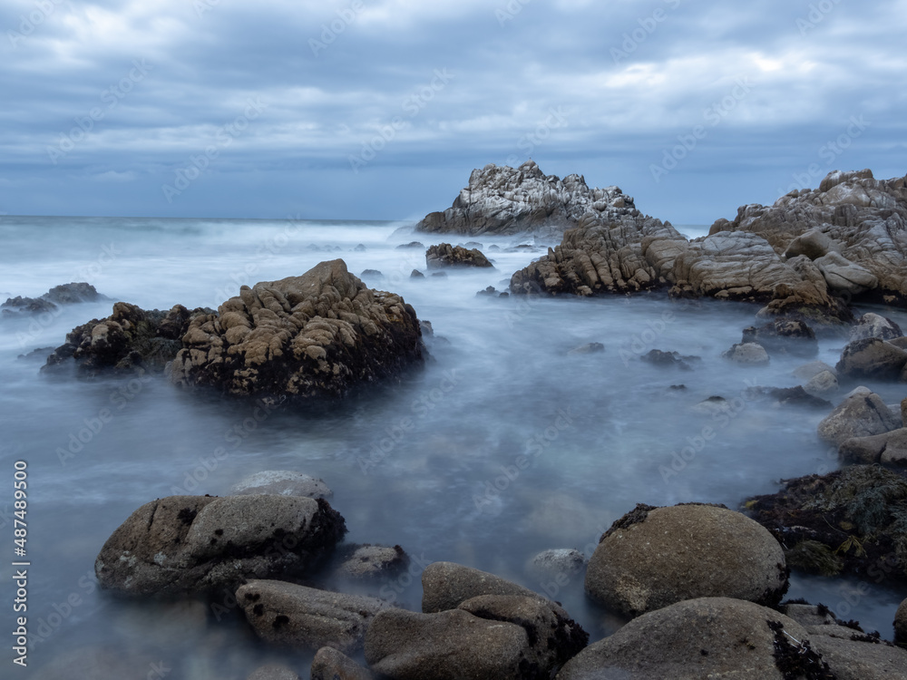 A rocky section of coastline near Monterey Bay in California, on an overcast day at sunset, long exposure.