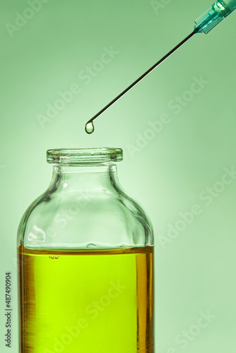 A drop of liquid drips from the needle of a medical syringe into the bottle. Front view. Macro photo.