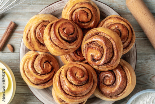 There is a plate with homemade fresh delicious cinnamon rolls, ingredients for their preparation and kitchen tools on the wooden table . Top view