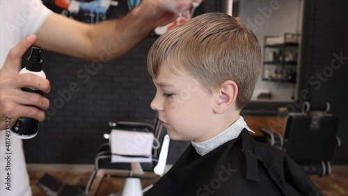 process of cutting a blond boy with a long braid in a chair in a barbershop salon, a barbershop concept for men and boys