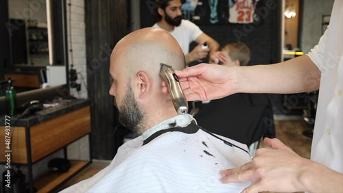 making hairstyle for man in a Barber shop, Latin American man gives a haircut to a bald bearded man in the barbershop salon