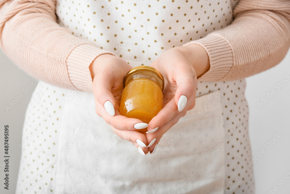 Woman holding jar of tasty orange jam on light background Woman holding jar of tasty orange jam on light background