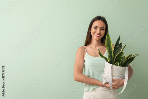 Young woman holding eco bag with houseplant on green background