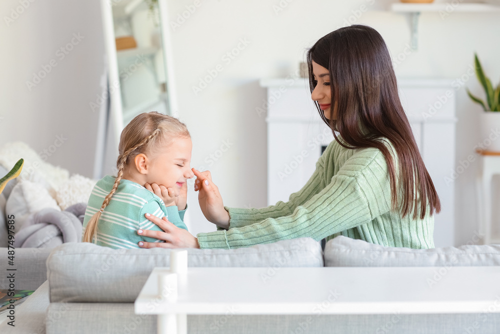 Happy mother touching her little daughter's nose at home