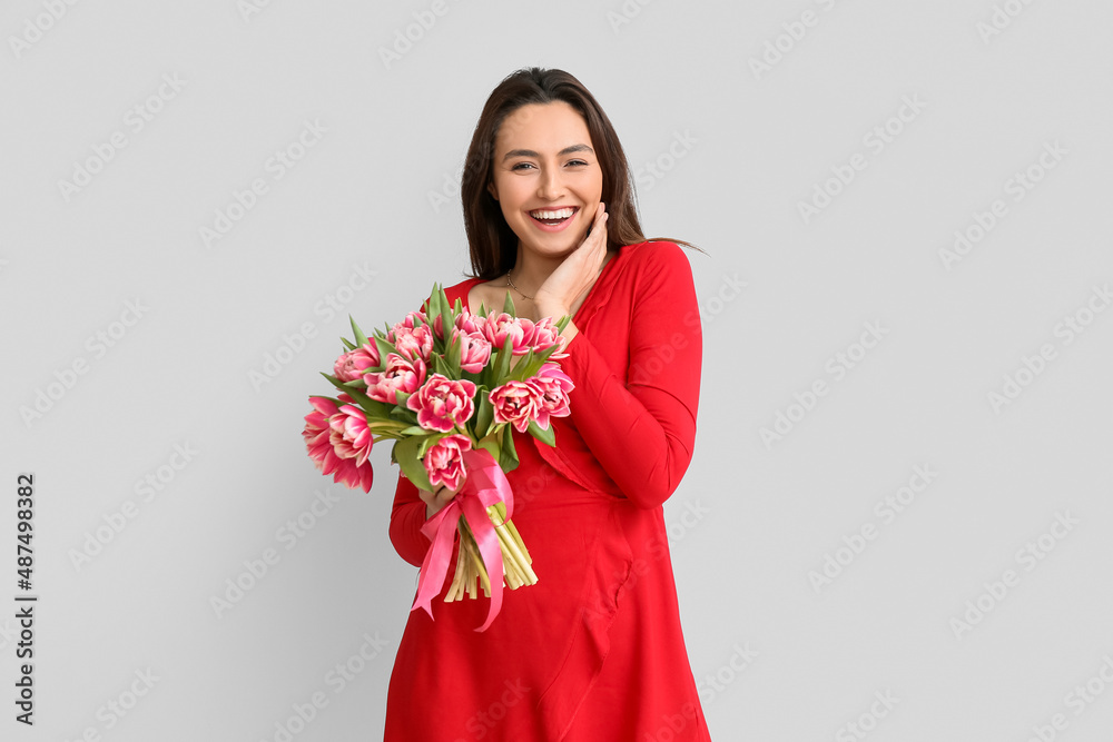 Beautiful young woman with bouquet of flowers on light background. International Women's Day celebration Beautiful young woman with bouquet of flowers on light background. International Women's Day celebration