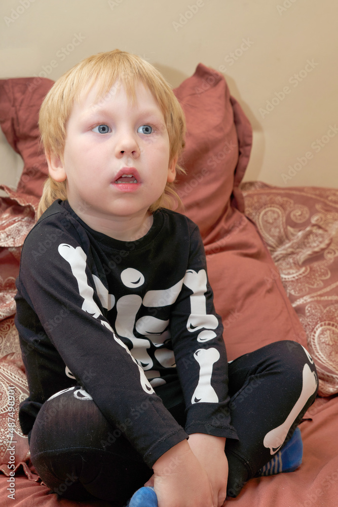 A child in a skeleton costume sits on the couch with an emotion on his face A child in a skeleton costume sits on the couch with an emotion on his face