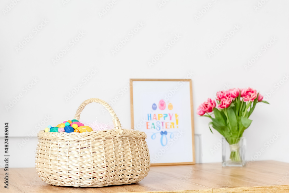 Basket with Easter eggs on table near light wall Basket with Easter eggs on table near light wall