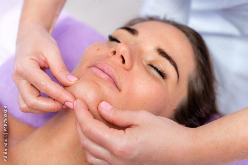 Relaxing massage. European woman getting facial massage in spa salon, side view
