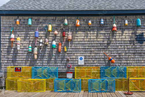 The gray plank wall of a traditional home is adorned with old floats and lobster traps as a symbol of a New England fishing village by the Atlantic Ocean. photo