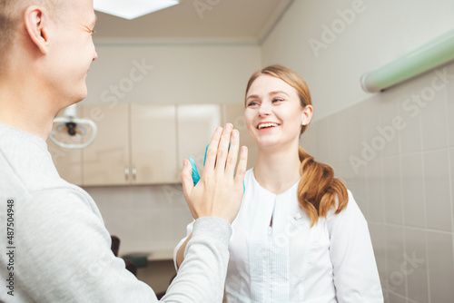 Beautiful female dentist in office in clinic, satisfied happy client shakes hands, excellent professional service. Clap