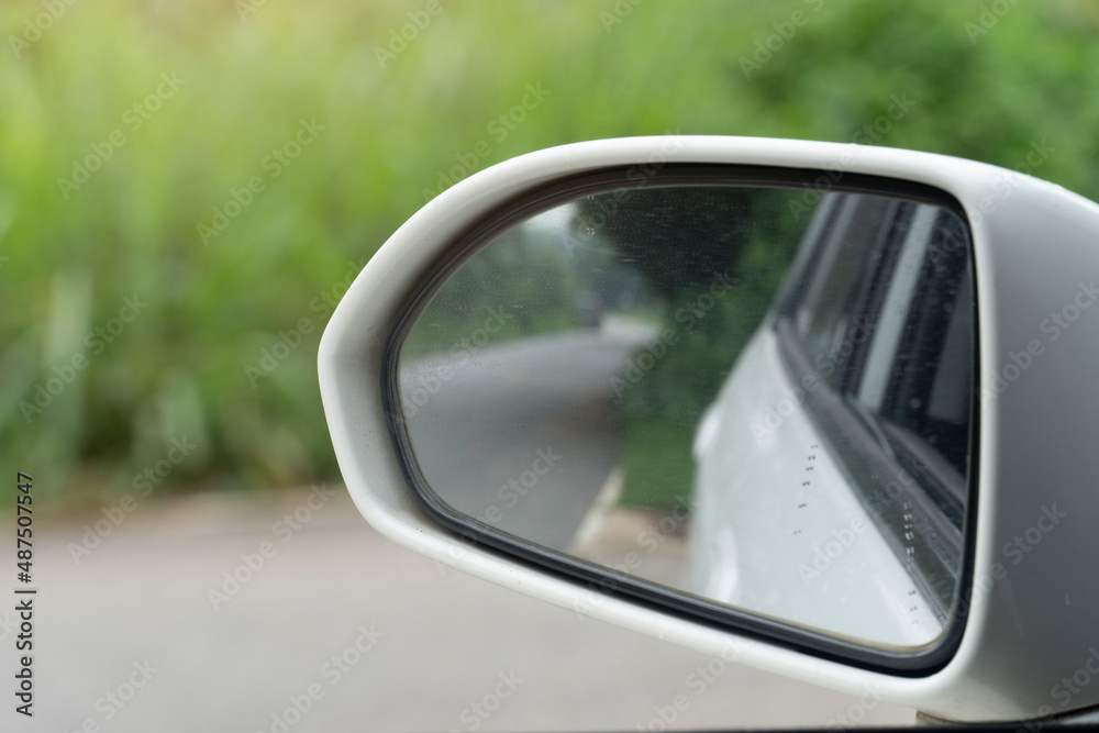 Close-up white frame of mirror wing of car. With asphalt road reflection from glass. Blurred of green grass beside the road.