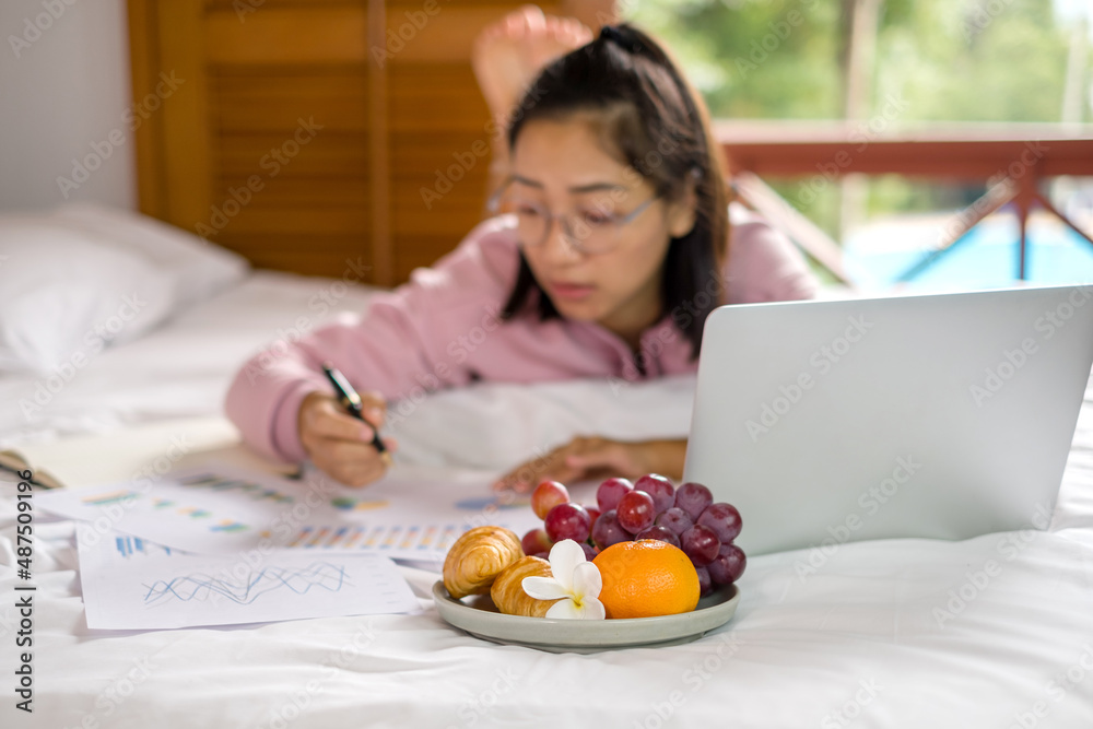 work from home, a young Asian woman who works in finance at home calculates financial graphs showing the results of his investments, planning the steps of his business growth