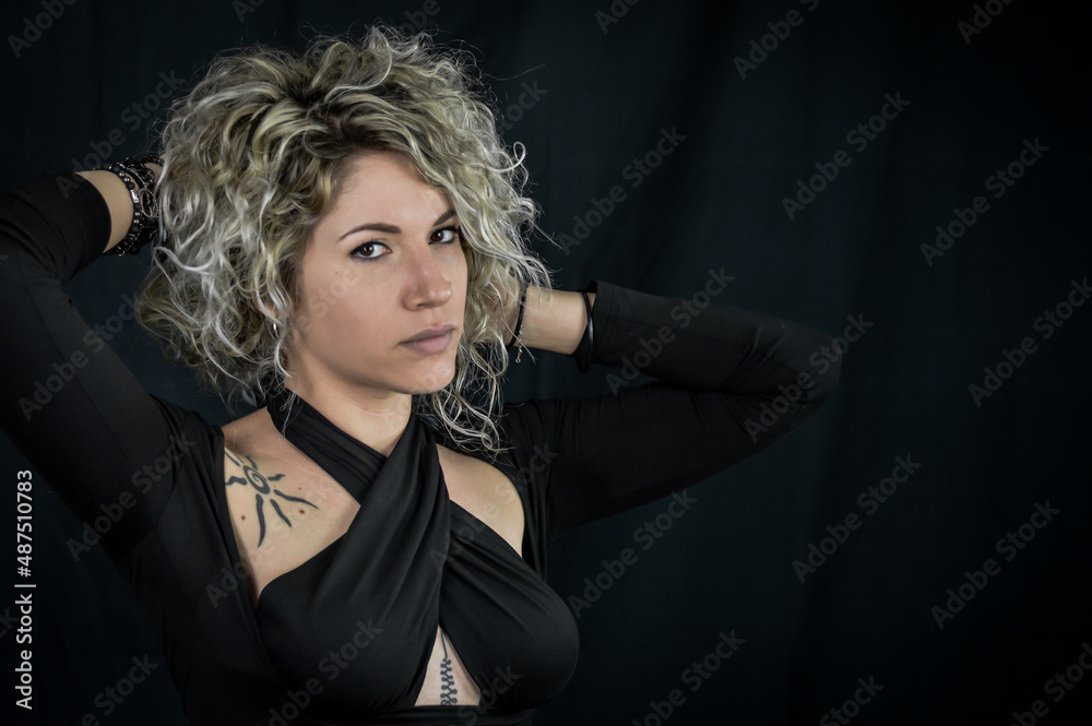 Portrait of a beautiful young curly blonde woman who, smiling, adjusts her hair and looks seductively, on black with space for text