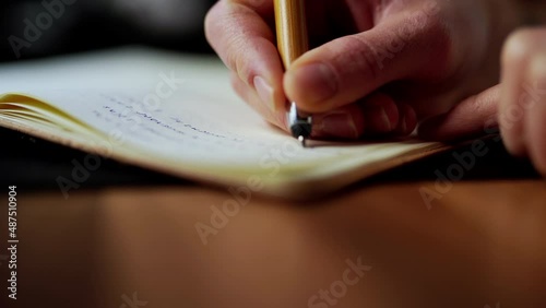 Caucasian right hand holding modern ink pen writing new idea on paper notebook journal. Extreme close up study, creativity, home working concept photo