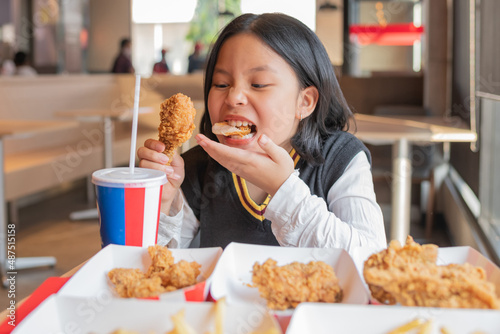 Close up portrait of a satisfied pretty  little asian girl eating fried chicken and french fries In the restaurant. Unhealthy food concept  close up