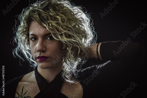 Backlit portrait of a curly blonde woman with eyeglasses who is adjusting the hair behind her head