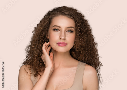 Curly long brunette hair young woman touching face beauty female portrait. Color backgound pink