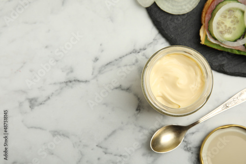 Jar of delicious mayonnaise near fresh sandwich on white marble table, flat lay. Space for text
