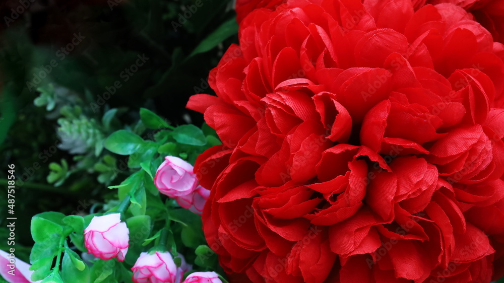 Red artificial flowers on a dark background. For background work with copy space. Selective focus