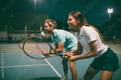 Tennis sport people concept. Mixed doubles player hitting tennis ball with partner standing near net